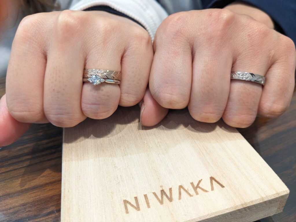 NIWAKAの婚約指輪と結婚指輪をつけたカップル、白鈴、花匠の彫