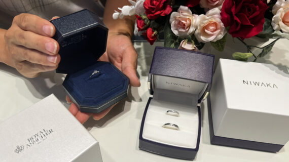 ロイヤル・アッシャーの婚約指輪が入ったケースを持つ男性とNIWAKA（ニワカ）の結婚指輪