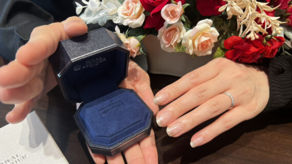 ロイヤル・アッシャーの結婚指輪を着けた女性の手元と箱を持つ男性の手元