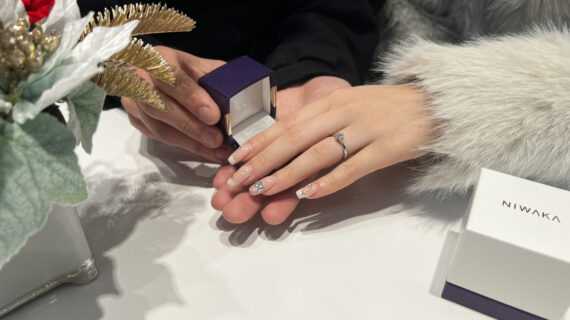 NIWAKA（ニワカ）の婚約指輪を着けた女性の手元とケースを持つ男性の手元