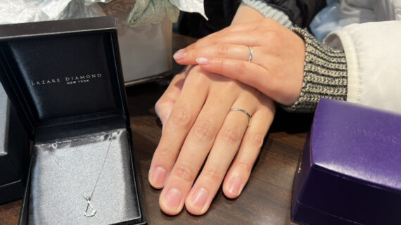 箱に入ったラザールダイヤモンドの婚約ネックレスとNIWAKA（ニワカ）の結婚指輪を着けたカップルの手元