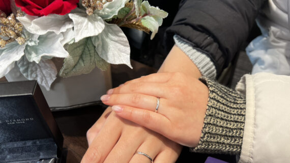 箱に入ったラザールダイヤモンドの婚約ネックレスとNIWAKA（ニワカ）の結婚指輪を着けたカップルの手元